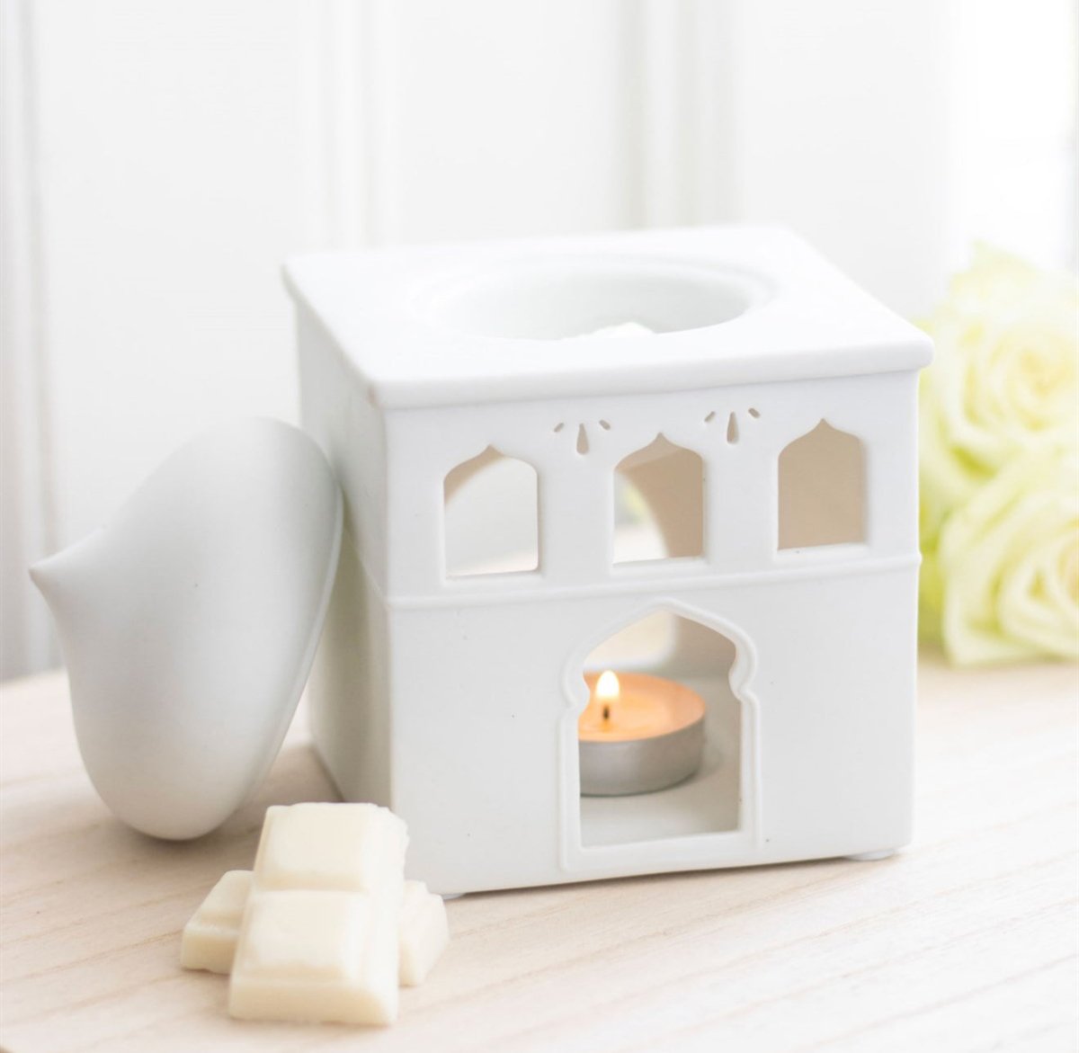 White ceramic lantern with a lit candle inside on a light surface.