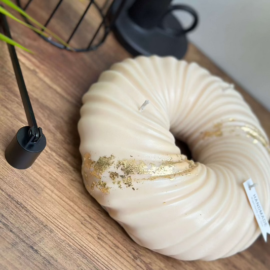 A cream, sculptural Halo luxury soy candle with gold accents, placed on a wooden surface.
